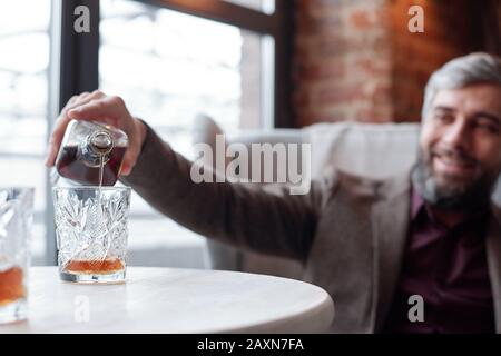Nahaufnahme des glücklichen Mannes, der Whisky in Glas gießt, während er in der Lounge-Bar ruht Stockfoto