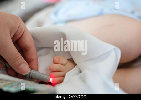 Der Arzt führt eine Lasertherapie am Zehenbereich der Babypatienten im Rehabilitationszentrum durch. Lasertherapie mit niedrigem Niveau. Biostimulation. Behandlung von Störungen Stockfoto