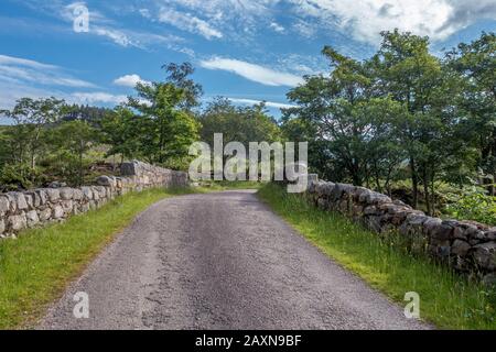 Gepflasterte Straße im Tal Glen Etive in den schottischen Highlands, die im Sommer über eine alte Steinblockbrücke mit Steinmauern an den Seiten führt Stockfoto