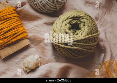 Macrame Seile in verschiedenen Farben, Draufsicht. Senf-, Oliven- und weiße Häkelfäden in wunderschöner Pastellkulisse, flaches Laienbild Stockfoto