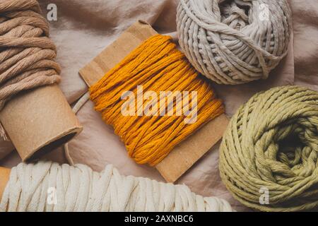 Macrame Seile in verschiedenen Farben, Draufsicht. Senf, rot, oliv und weiß gehäckelte Fäden in schöner Pastellkulisse, flaches Laienbild Stockfoto