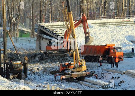 Bagger lädt Erde in einen LKW an einer Baustelle und Lkw-Kran arbeitet im Winter in Russland an einer Baustelle. Stockfoto