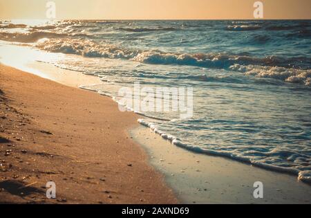 Die Sonne spiegelt sich in Wellen wider, die auf einem nahe gelegene Sandstrand rollen Stockfoto