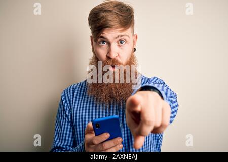 Rotkopf Iren mit Bart mit Smartphone auf den Bildschirm über dem isolierten Hintergrund zeigen mit dem Finger auf die Kamera und zu Ihnen, Handzeichen, Pos Stockfoto