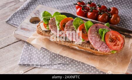 Lebensmittelbanner. Bruschetta mit Salami und Tomaten, Frischkäse, Erbsenmikrogreens und Pesto auf einem Holzschneidebrett Stockfoto