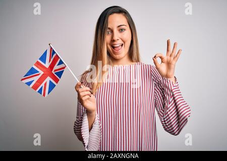 Junge, schöne blonde Frau mit blauen Augen, die die flagge des vereinigten Königreichs hält, die mit den Fingern ein gutes Zeichen macht, ein hervorragendes Symbol Stockfoto