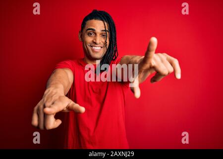 Junger, gutaussehender afro-amerikanischer afro-Mann mit Dreadlocks mit rotem Casual-T-Shirt, das auf Sie und die Kamera mit den Fingern zeigt, lächelnd positiv und Stockfoto