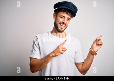 Junger Fahrer mit Bartehut, der über einem isolierten weißen Hintergrund steht und lächelt und die Kamera mit zwei Händen und Fingern betrachtet Stockfoto