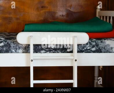 Weißer Holzstuhl in der Nähe eines Holzbettes mit Decken Unter den Lichtern Stockfoto