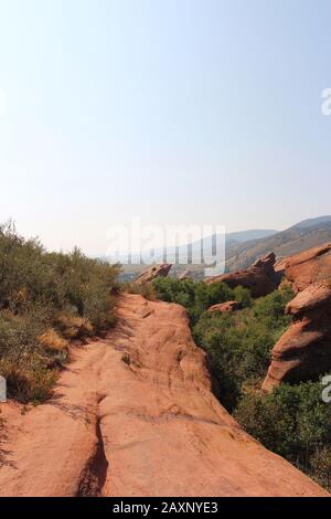 Der Trading Post Trail neben großen Felsformationen aus rotem Sandstein mit Sträuchern, die in den Rissen im Red Rocks State Park, Morrison, Colorado wachsen Stockfoto