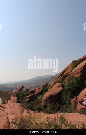 Ein Pfad neben großen Felsformationen aus rotem Sandstein mit Sträuchern, die in den Rissen auf dem Trading Post Trail im Red Rocks State Park, Morrison, wachsen Stockfoto