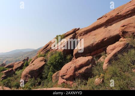 Große Felsformationen aus rotem Sandstein mit Sträuchern, die in den Rissen auf dem Trading Post Trail im Red Rocks State Park, Morrison, Colorado wachsen Stockfoto