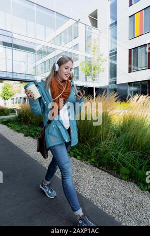 Junge Frau mit Ohrhörer vor dem Bürogebäude Stockfoto