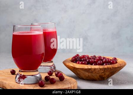 Zwei Gläser mit hausgemachtem, frisch gepresstem Preiselbeersaft und eine Schüssel mit Preiselbeeren auf einem grauen Betontisch. Stockfoto