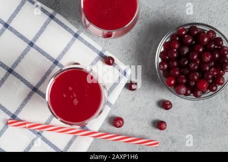 Zwei Gläser mit hausgemachtem, frisch gepresstem Preiselbeersaft und eine Schüssel mit Preiselbeeren auf einem grauen Betontisch, Draufsicht, flacher Lay. Stockfoto