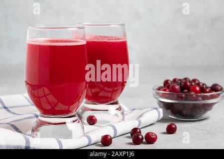 Zwei Gläser mit hausgemachtem, frisch gepresstem Preiselbeersaft und eine Schüssel mit Preiselbeeren auf einem grauen Betontisch. Stockfoto