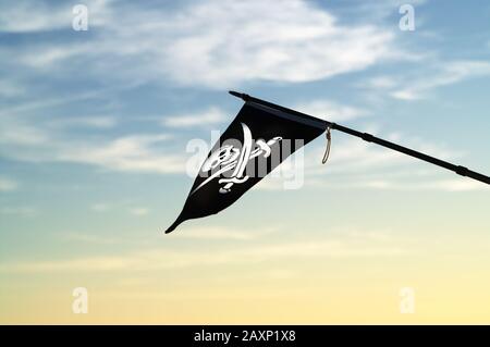 Jolly Roger (Piratenfahne) im Wind gegen den bunten Abendhimmel mit Wolken Stockfoto