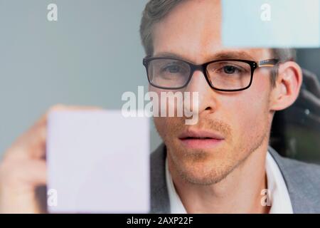 Junger Geschäftsmann liest Haftnotiz in der Fensterscheibe, Porträt Stockfoto
