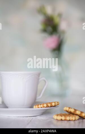 Kaffeetasse mit Keksen vor hellem Hintergrund, Blumen im Hintergrund Stockfoto