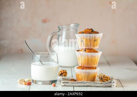 Glas Milch, Vanillekaramel-Muffins in Papierbecher und Milchflaschen auf weißem Holzhintergrund. Köstlicher Cupcake. Hausgemachte Biskuitkuchen. Stockfoto