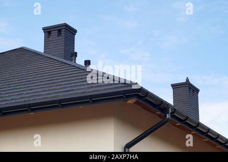 Ein neu errichtetes Wohnhaus. Ein Dachfragment aus Metalldachziegeln, neue Schornsteine. Stockfoto