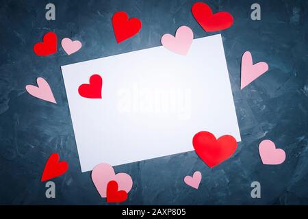 Draufsicht auf leere Grußkarte mit Kopierbereich auf blauem, abstraktem, strukturiertem Hintergrund mit verstreuten, handgefertigten roten und rosafarbenen Herzen Stockfoto