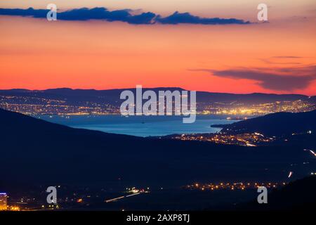 Panorama der Novorossijsk Bay nachts vom Kaukasusgebirge. Helle Lichter, Spiegelung im Wasser. Autoleuchten, Berge. Straßen. Dunkelblaues p Stockfoto