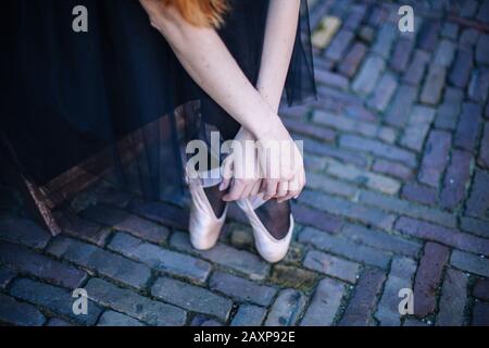 Nahaufnahme der Füße der Ballerina in pointe auf der Straße. Die Beine der Ballerina sind stark angepaßt. Junge Ballerina-Frau mit roten Haaren im Balletttrend und pointe Stockfoto