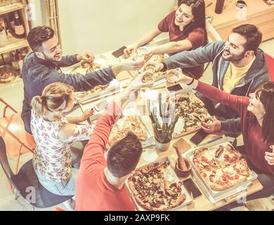 Fröhliche Freunde, die zu Hause Bier toben und Pizza in Papierbox essen - Junge Leute haben Spaß beim gemeinsamen Trinken und Lachen - Abendessen, Party und Freunde Stockfoto