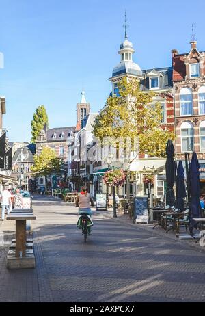 Venlo, Limburg-Niederlande - 13. Oktober 2018: Straße mit Cafés, Restaurants und Bars im historischen Zentrum der niederländischen Stadt. Frau, die mit dem Fahrrad unterwegs ist. Stadtradfahren. Stockfoto