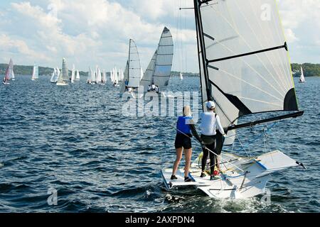 Kinder Segeln kleines Boot mit einem Blick auf ein Schlauchboot im Vordergrund mit vielen anderen Booten im Hintergrund bei einer Binnenseeregatta Stockfoto