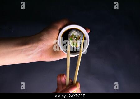 Stöcke rasieren die Rolle von Mohn über einen Teller Sojasoße, eine Platte in einer schönen weiblichen Hand über einem schwarzen Hintergrund Stockfoto