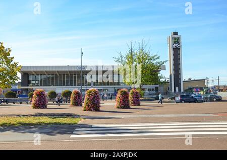 Venlo, Limburg-Niederlande - 13. Oktober 2018: Zebraübergang und Gehweg führen zum Hauptgebäude des Bahnhofs in der niederländischen Stadt. Blumenschmuck, geparkte Autos, Menschen auf der Straße. Stockfoto