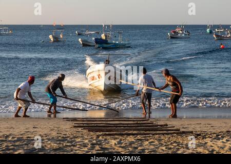 Puerto Escondido, Oaxaca, Mexiko - Fischerboote kommen im Morgengrauen am Hauptstrand von Puerto Escondido an, um gefangenen Fisch zu verkaufen. Der Kapitän lenkt den Bo Stockfoto