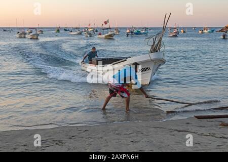 Puerto Escondido, Oaxaca, Mexiko - Fischerboote kommen im Morgengrauen am Hauptstrand von Puerto Escondido an, um gefangenen Fisch zu verkaufen. Der Kapitän lenkt den Bo Stockfoto
