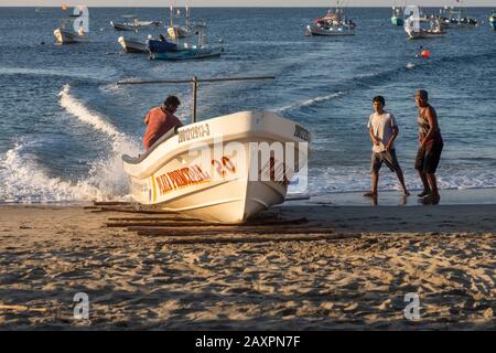 Puerto Escondido, Oaxaca, Mexiko - Fischerboote kommen im Morgengrauen am Hauptstrand von Puerto Escondido an, um gefangenen Fisch zu verkaufen. Der Kapitän lenkt den Bo Stockfoto