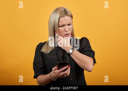 Mädchen in schwarzem Kleid verärgerte Frau sieht aus und ärgert sich am Telefon Stockfoto