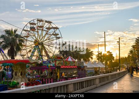 Blick auf die Promenade von Sanremo mit dem Panoramarad und den Karussells im Vergnügungspark am Ufer bei Sonnenuntergang, Ligurien, Italien Stockfoto