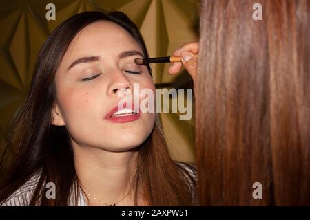 Make-up-Künstlerin Mexican Brunette Frau Stylist mit Schatten vorsichtig mit einem Pinselschatten auf die Augenlider einer kaukasischen Frau in Mexiko Stockfoto