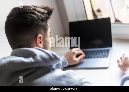 Rückansicht eines jungen Mannes, der mit einem Laptop auf dem Desktop arbeitet Stockfoto