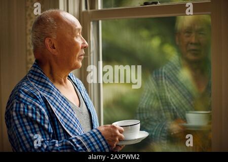 Ein älterer Mann in seinem Morgenmantel starrt auf seine Reflexion. Stockfoto