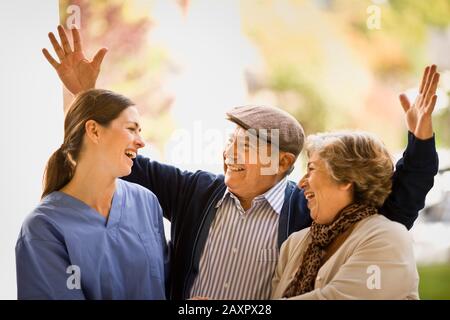 Weibliche Krankenschwester und Senior paar Lachen und Reden, als ein älterer Mann seine Arme wirft. Stockfoto
