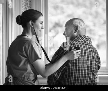 Weibliche Krankenschwester überprüft den Herzschlag eines älteren Mannes mit einem Stethoskop. Stockfoto