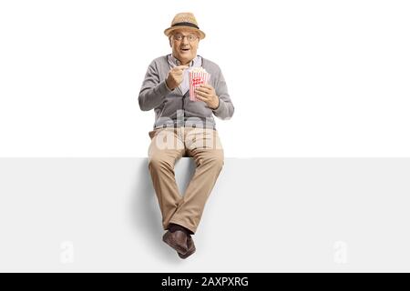 Aufgeregter reifer Gentleman, der auf einer Platte sitzt, die Popcorn isst, isoliert auf weißem Hintergrund Stockfoto