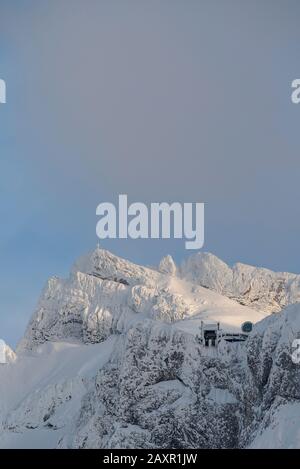 Der Kopfbahnhof der Karwendelbahn, und im Hintergrund der Gipfel der westlichen Karwendelspitze am letzten Abend leicht mit Lichtwolken. Stockfoto