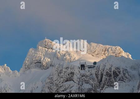 Der Kopfbahnhof der Karwendelbahn, und im Hintergrund der Gipfel der westlichen Karwendelspitze am letzten Abend leicht mit Lichtwolken. Stockfoto