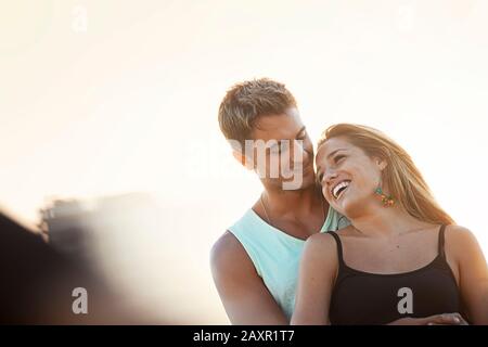 Lächelnder junger Mann steht mit seinen Armen um eine lächelnde junge Frau. Stockfoto