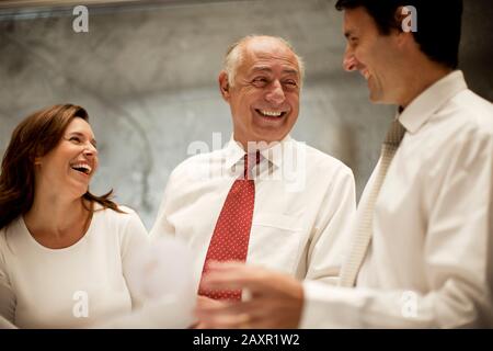 Junge Geschäftsfrau und Geschäftsfrau lachen, während sie mit einem älteren männlichen Kollegen sprechen. Stockfoto