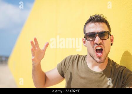 Wütend rüde junger gutaussehender Mann, der über weißen Hintergrund schreit. Stockfoto