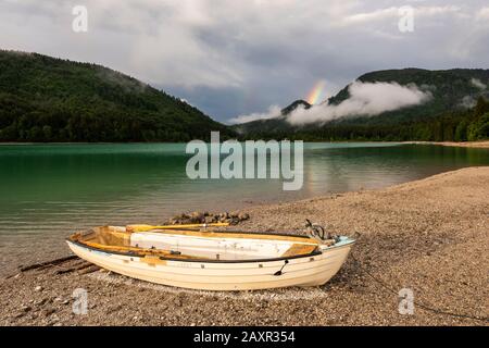 Einsames Fischerboot am Ufer des Walchensees, im Hintergrund ein Regenbogen über dem Rhombus Stockfoto